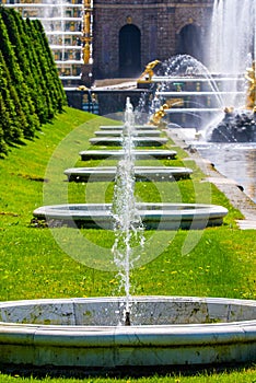 Row of fountains on green grass, garden background