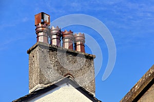 Row of four old ornate ceramic chimney pots on a rooftop chimney stack, with blue sky