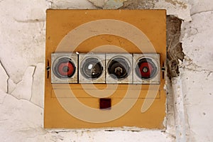 Row of four old vintage disconnected ceramic fuse holders with missing fuses on front side of yellow plastic box on cracked wall