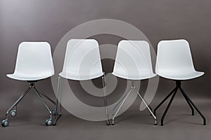 Row of four white plastic chairs isolated on gray background. Furniture series.