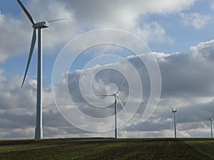 Row of four wind turbines with cottony clouds in a blue sky