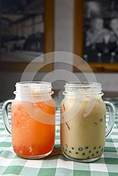 Row of fresh boba bubble tea glasses on wooden table with green plaid tablecloth background.