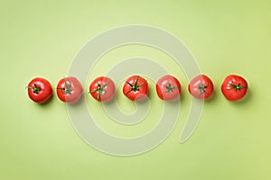 Row of fresh red tomatoes on green background. Top view. Copy space. Minimal design. Vegetarian, vegan, organic food and