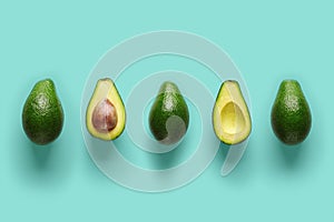 Row of fresh wholes and halves of organic avocado with kernels in center on blue backgrond. Top view