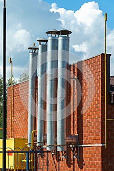 A row of galvanized steel chimney pipes on the facade of a brick boiler house building