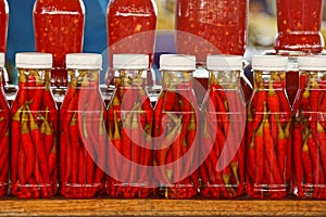 A row of glass jars with canned red pepper on the display shelf