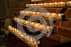 Row of glowing candles in church. Candles with flame on dark background. Faith and religion concept. Candles in catholic church.