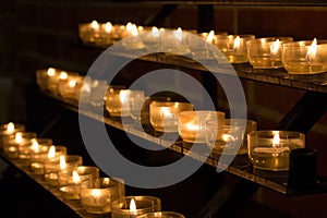 Row of glowing candles in church. Candles with flame on dark background. Faith and religion concept. Candles in catholic church.