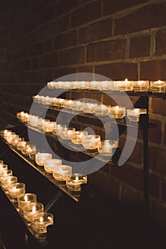 Row of glowing candles in church. Candles with flame on dark background. Faith and religion concept. Candles in catholic church.