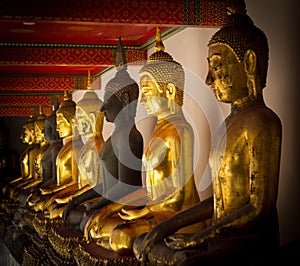 Row of golden and dark seated buddhas in a Buddhist temple