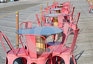 A row of granite tables with pink chairs on a wooden boardwalk