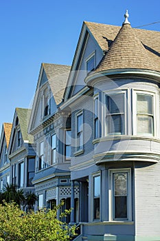 Row of gray housing buildings with light brown roofs on homes and Victorian style facades in shade with sun streak on