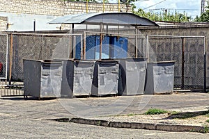 A row of gray iron dumpsters stand on the asphalt