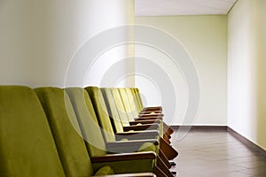 Row of Green Auditorium Seating Soft Chairs with Writing Pads Placed along the Wall in the Hallway. Business or Political Event,