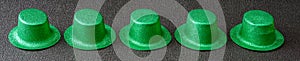 Row of green glitter leprechaun hats on a black background, happy St. Patrick’s Day