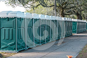 Row of green porta portable potty outhouses ready for use at a concert, festival, or event