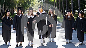 Row of happy young people in graduation gowns outdoors. Students are walking in the park.