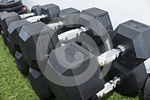 A row of hex dumbbells laid on an artificial grass mat. Workout equipment at a home gym