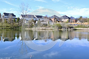 Row of homes along lakeshore with tree and cloud reflections across water surface