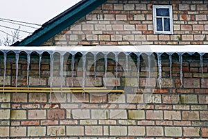 Row of icicles from a roof on a brick wall at home