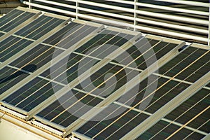 Row of industrial photovoltaic or solar pannels on side of building with metal gaurd rail at thirty degree angle for sun photo