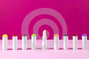 Row of lip balms hygienic lipsticks on multicolored background. Varied balm flavors are marked with different colors on tube