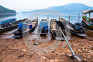 A row of long-tailed boats mooring on the beach with mountains background on a cloudy day.