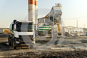 Row many modern big mixer trucks parked against mobile temporary concrete plant factory at new asphalt road construction site