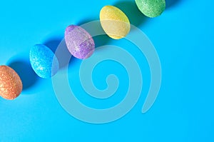 Row of many scattered colorful eggs with glitters lies on blue table on kitchen. Easter concept