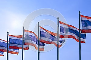 Row of many Thai flags on flagpoles waving in the wind against blue clear sky background