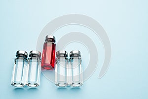 A row of medical vials. Glass bottles with a transparent medicine and one with red.