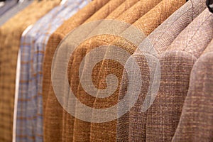 A row of men\'s suits, jackets hanging on a rack for display