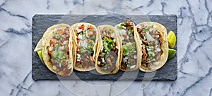 Row of mexican street tacos on slate with carne asada and al pastor in corn tortilla photo