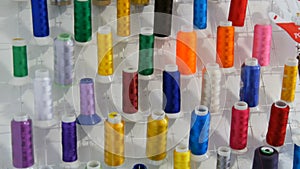 A row of multi-colored different threads for a sewing machine and overlock in a sewing workshop or atelier. Rows spools