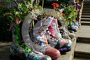 Row of multi-coloured leather painted boots with flowers growing in them