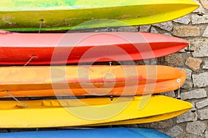 Row of multicolored kayaks against stonewall background