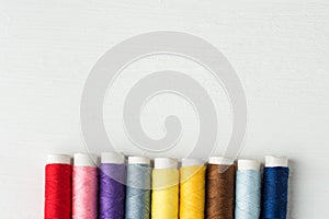 Row of multicolored rainbow palette sewing threads on cardboard spools. White wood background. Crafts hobbies artisan business