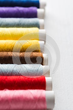 Row of multicolored sewing threads on cardboard spools. White wood background. Crafts hobbies local artisan business