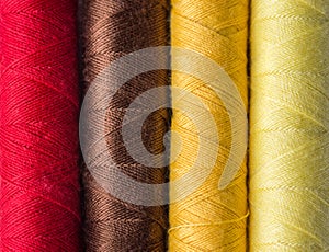 Row of multicolored sewing threads on of warm color palette red brown yellow. Textured background backdrop for crafts hobbies
