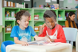 Row of multiethnic elementary students reading book in classroom.