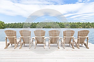 Row of Muskoka chairs on a dock looking onto the lake.