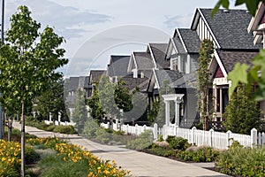 A row of new homes with a wide walkway and picket fences.