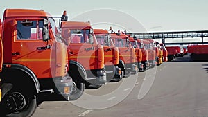 Row of new trucks standing on a concrete surface on blue sky background. Stock footage. Mechanical engineering and