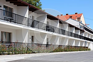 Row of newly built motel room balconies with black metal fences surrounded with decorative garden plants and concrete tiles