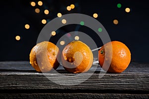 A row of orange clementines on a barn wood board with background lights on a black background
