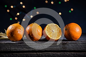 A row of orange clementines on a barn wood board with background lights on a black background
