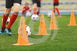 A row of orange soccer training cones. Players running with football balls between practice cones