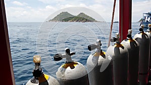 Row of oxygen tanks and diving equipment placed on modern boat in rippling ocean near Koh Tao resort, Thailand. Concept