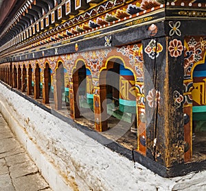 Row of painted turning prayer wheels mantra in Bhutan with traditional writing mantra which sounds as Om mani padme hum, literally