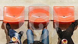 Row of plastic chairs and legs in football stadium.